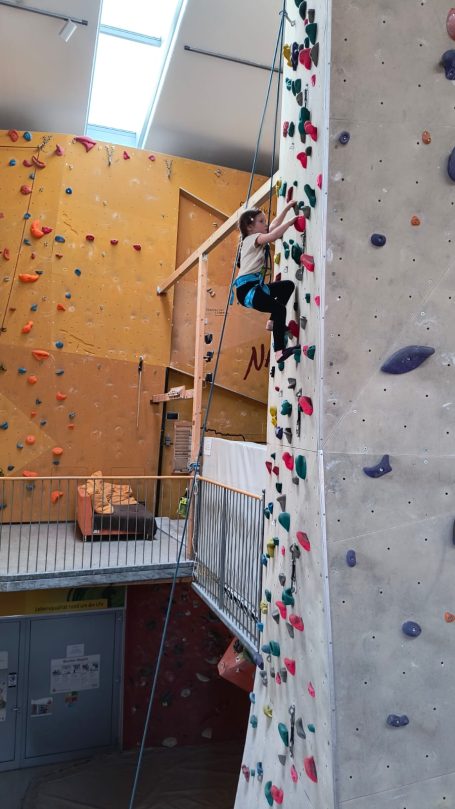 Junge klettert an einer bunten Kletterwand in einer Kletterhalle.