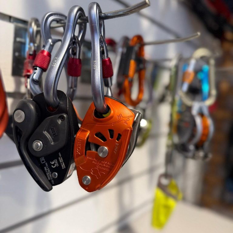 Kletterkurse für Beginner Sicherheitskarabiner und Bremsgeräte an einem Wandregal in einem Klettergeschäft.