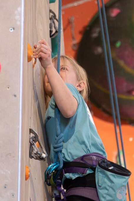 Ein Kind klettert an einer Kletterwand und erreicht einen Griff.