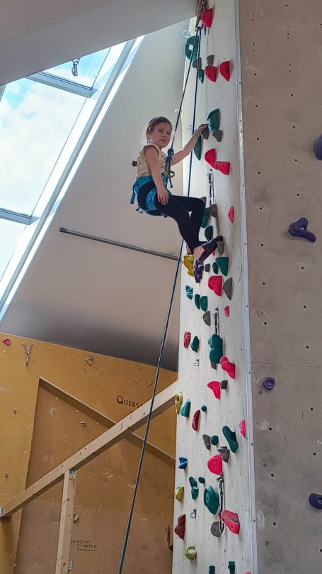 Ein Kind klettert an einer bunten Kletterwand in einem Innenraum.