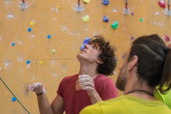 Junger Mann beim Bouldern, schaut nach oben, während er in der Wand klettert.