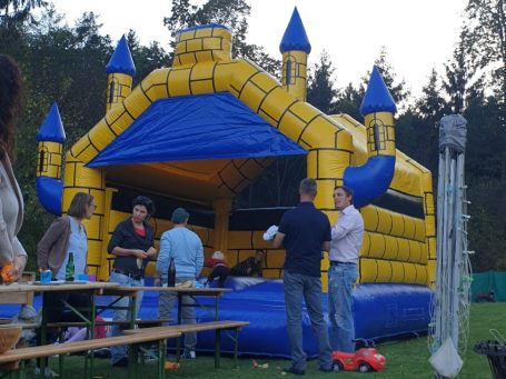 Bunte Hüpfburg mit Personen, die sich in der Nähe unterhalten und etwas essen.