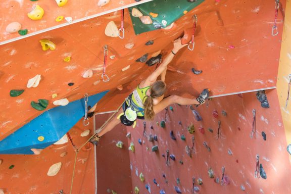 Junge klettert an einer orangefarbenen Kletterwand mit bunten Griffen.