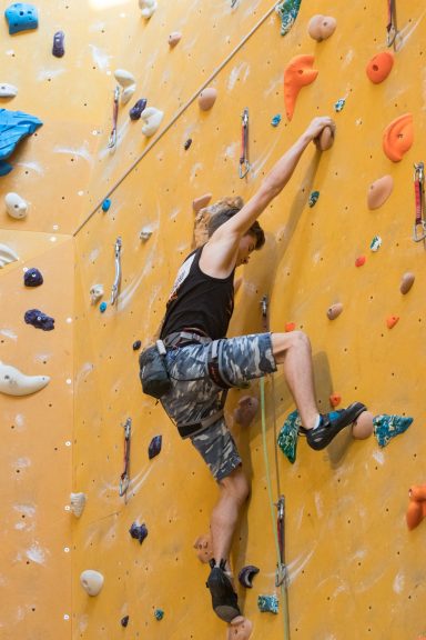 Person klettert an einer orangefarbenen Kletterwand mit bunten Griffen.