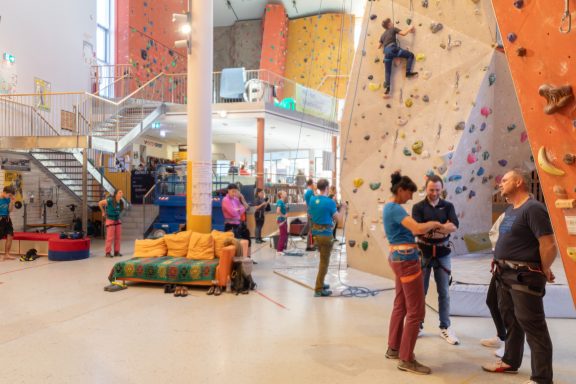 Kletterhalle mit mehreren Kletterwänden und Menschen, die klettern oder sich vorbereiten.