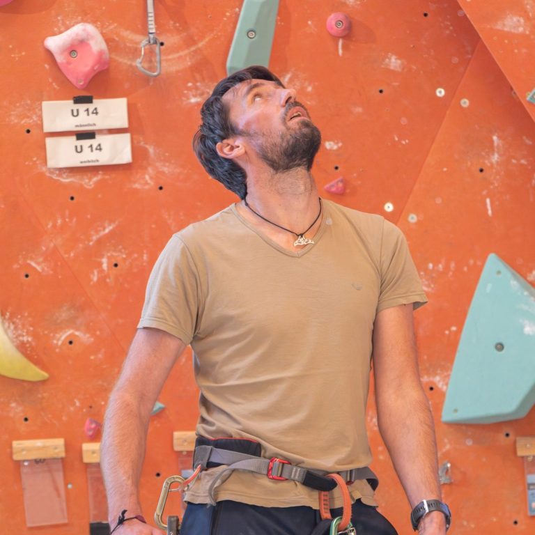 1-Tageskletterkurs Mann in Kletterausrüstung schaut nach oben auf eine Kletterwand.