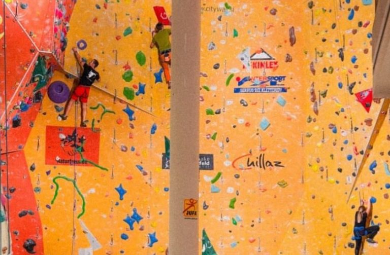 Kletterwand mit bunten Haltegriffen und Kletterern in einer Sporthalle.